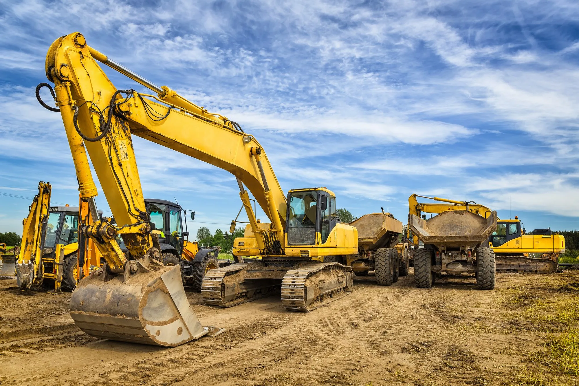 A fleet of heavy construction equipment — an excavator and dump trucks — staged at a job site